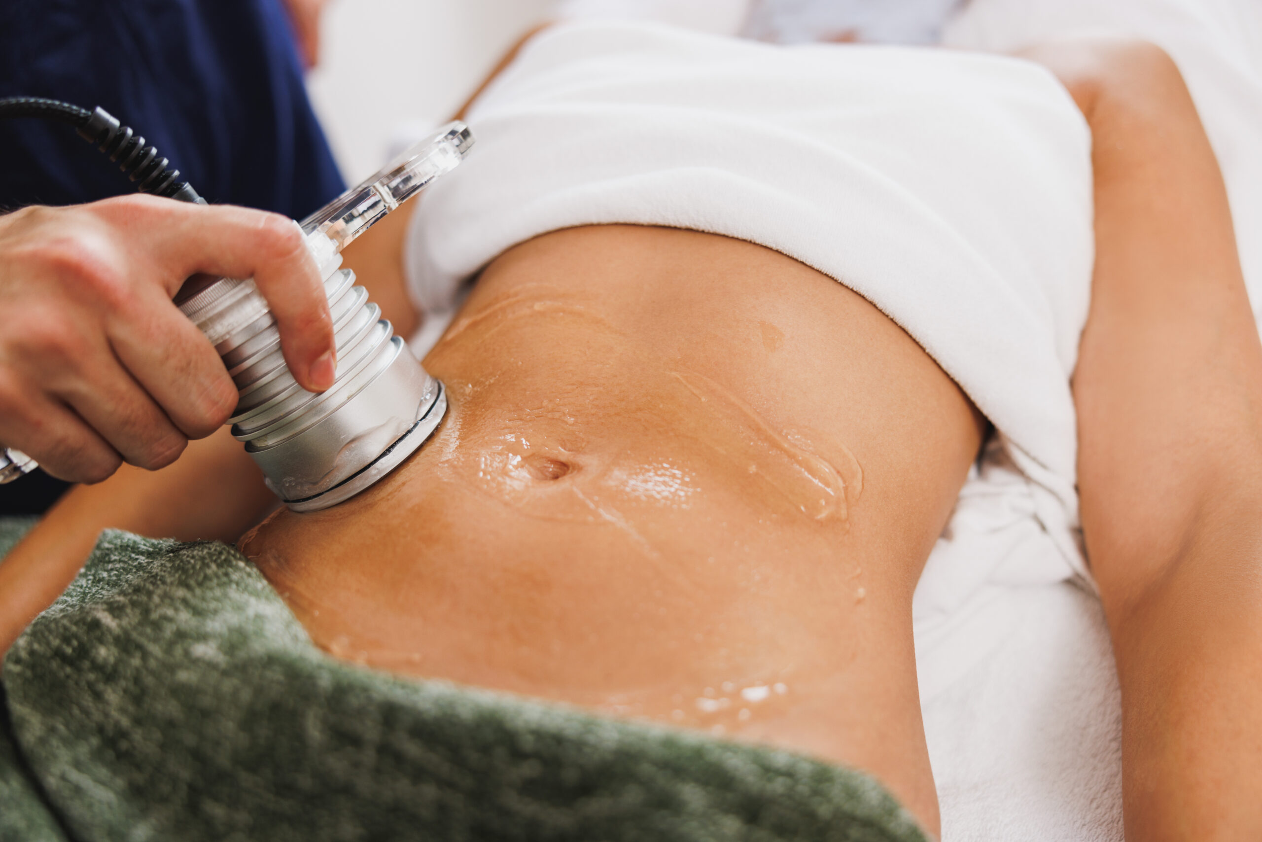 Unrecognizable woman getting an an ultrasound cavitation treatment to fat reduction on abdomen at the beauty salon.